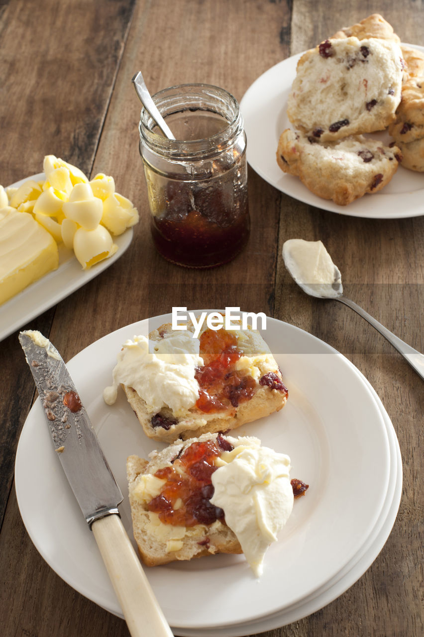 Fresh buttered rock cake with a dollop of whipped cream and fruit jam served on a white plate 