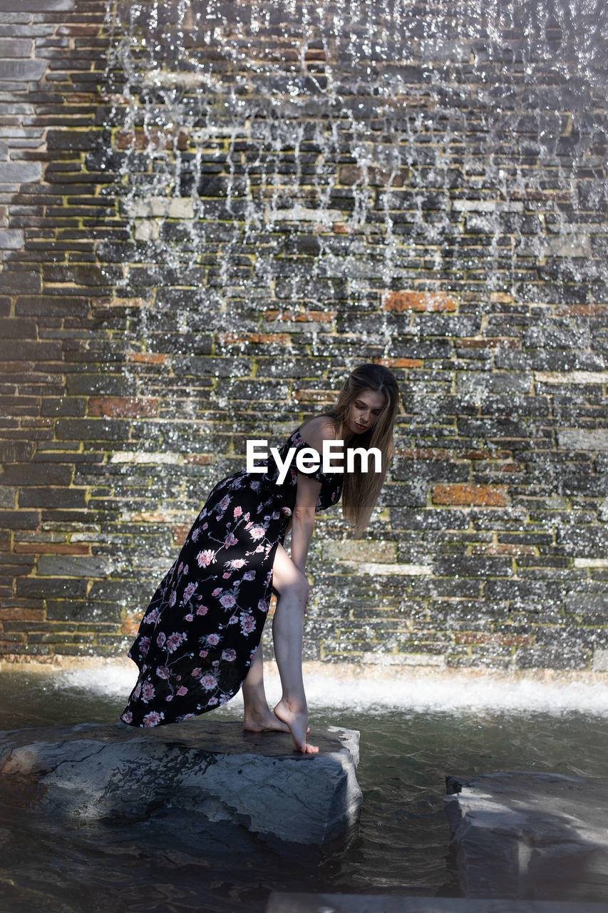 SIDE VIEW OF YOUNG WOMAN AGAINST WALL