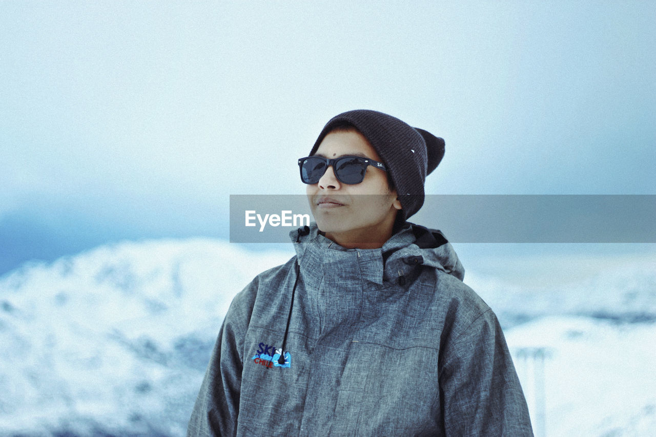 Woman wearing sunglasses and sweater standing against sky during winter