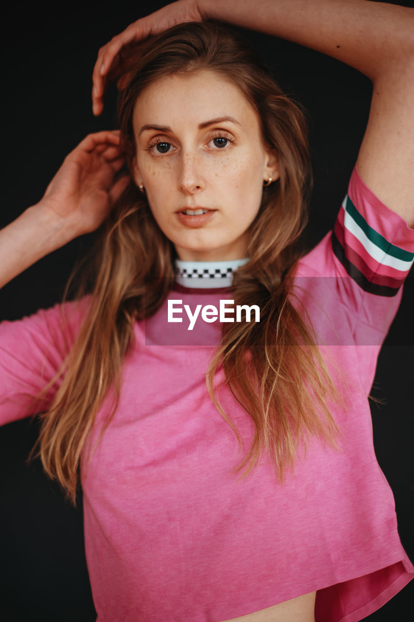 Portrait of beautiful young woman standing against black background