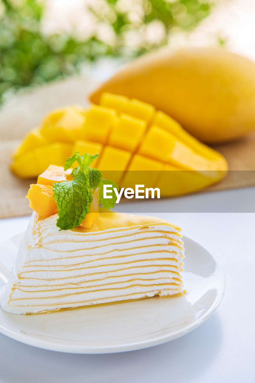 Close up mango crepe cake sliced on a white plate decorated with a piece of mango fruits 