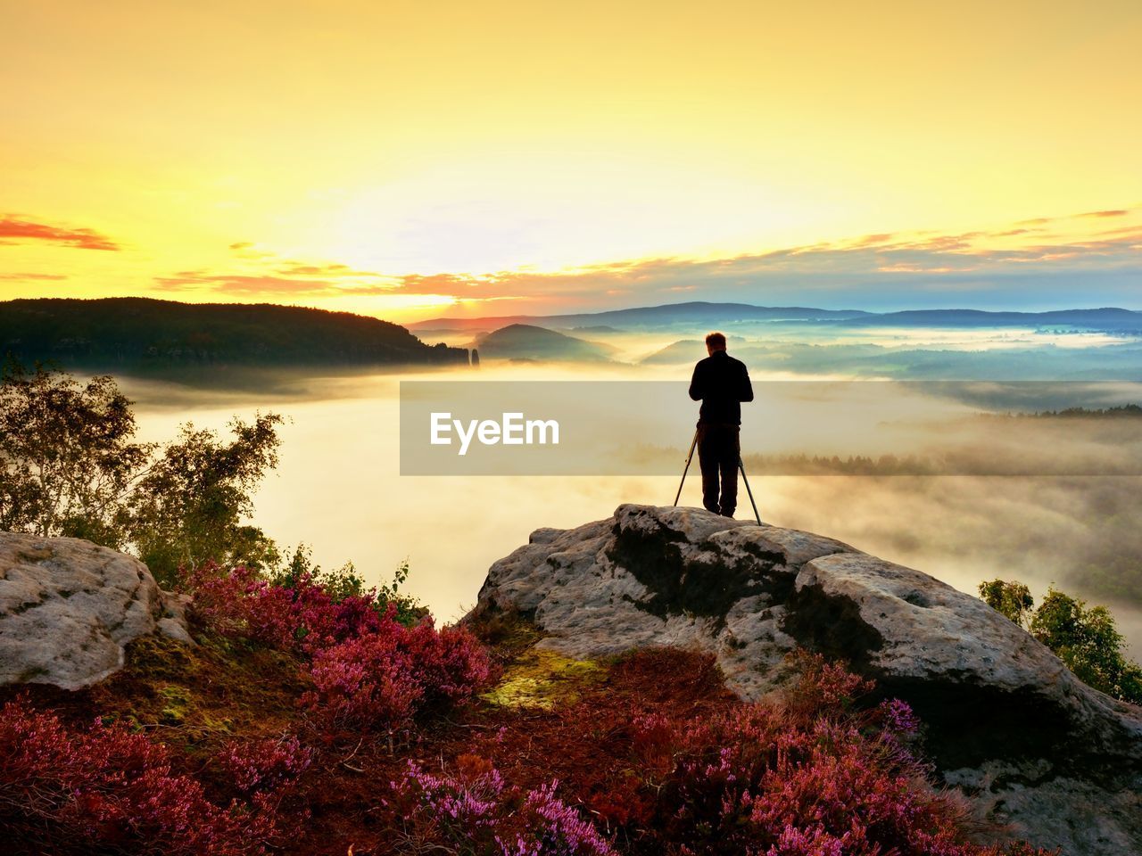 Professional photographer takes photos with mirror camera and tripod on peak of rock. dreamy nature