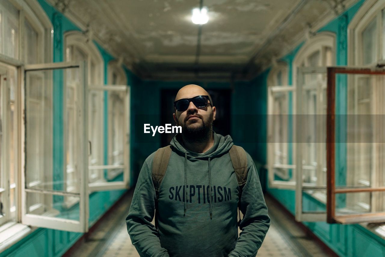 Portrait of man wearing sunglasses standing amidst open windows in corridor