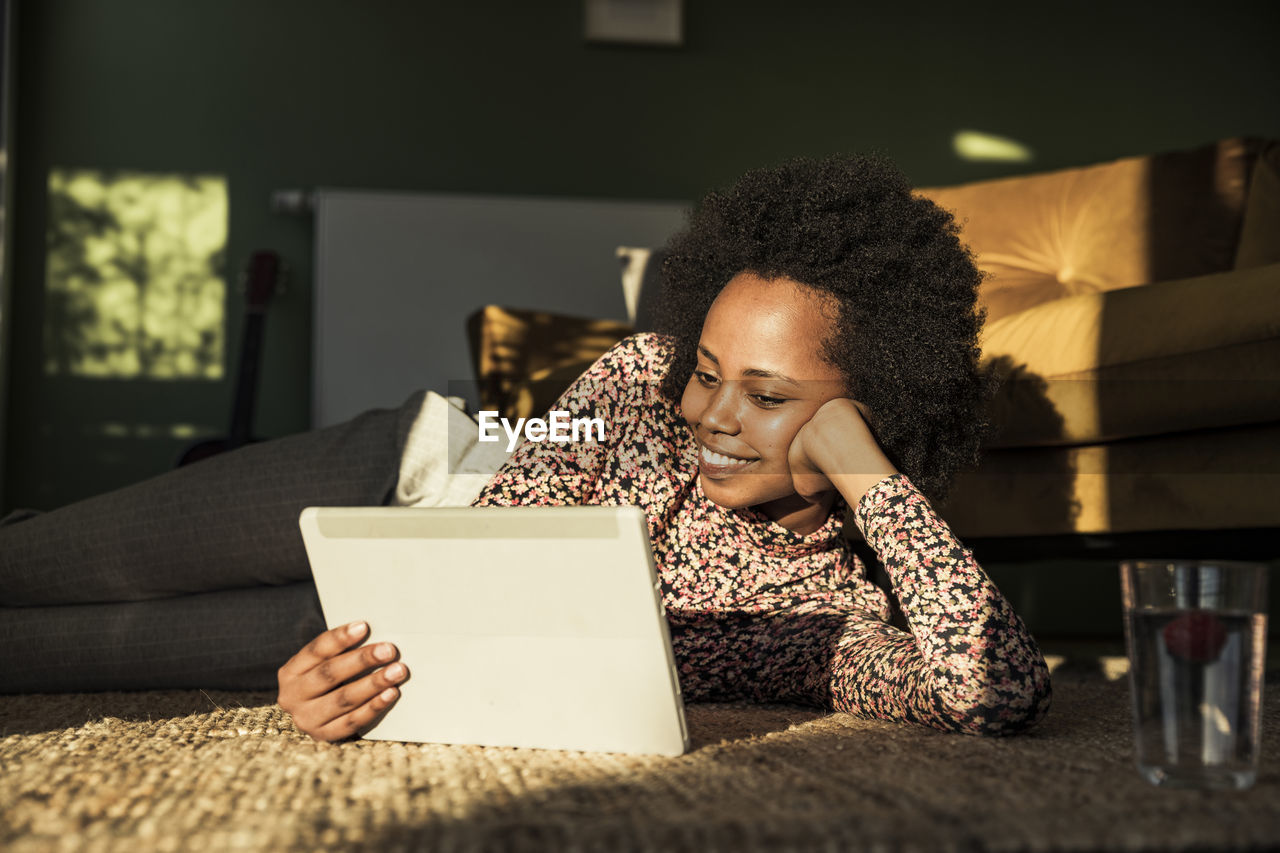 Smiling woman using digital tablet while lying on carpet