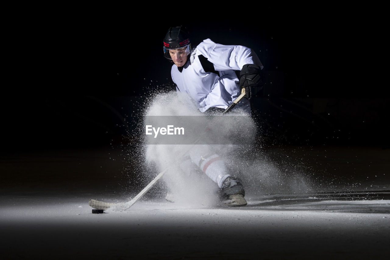 Man playing ice hockey against black background