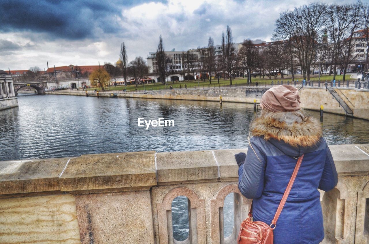 Rear view of woman standing against canal in city