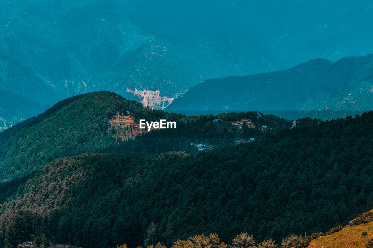 HIGH ANGLE VIEW OF TREES AND BUILDINGS AGAINST MOUNTAINS