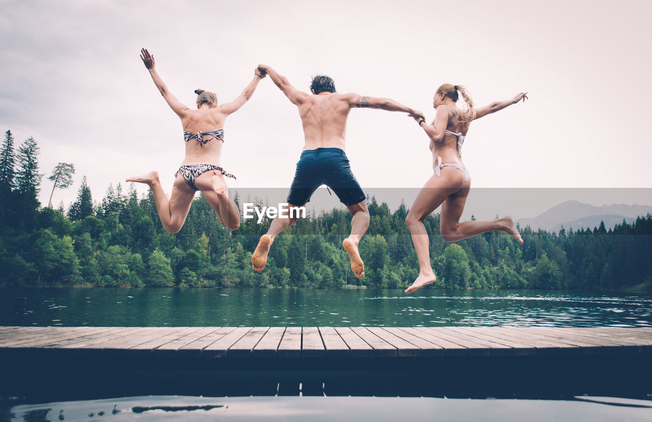 People jumping by lake against sky