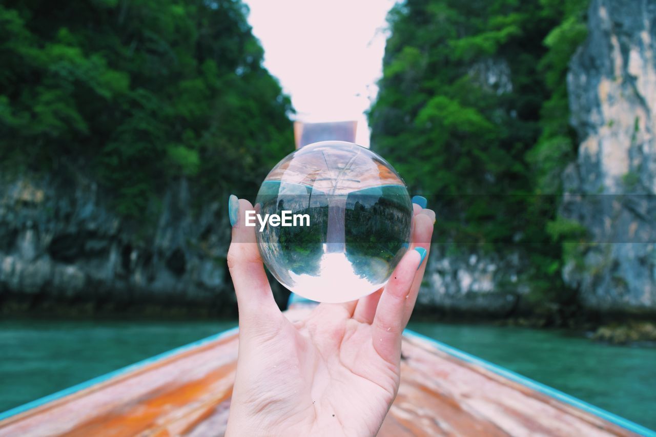 Cropped hand holding crystal ball with reflection on rocks on boat