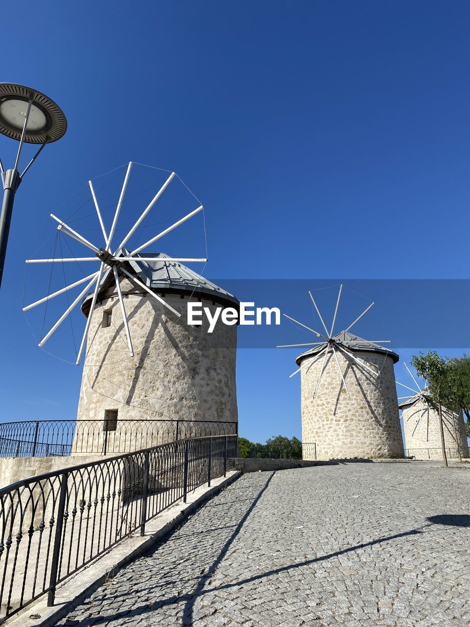 sky, windmill, architecture, clear sky, blue, built structure, wind, nature, renewable energy, low angle view, building exterior, alternative energy, environmental conservation, no people, wind power, day, wind turbine, sunny, turbine, power generation, technology, building, outdoors, sunlight, mill, tower, city, communication, environment, satellite dish, satellite