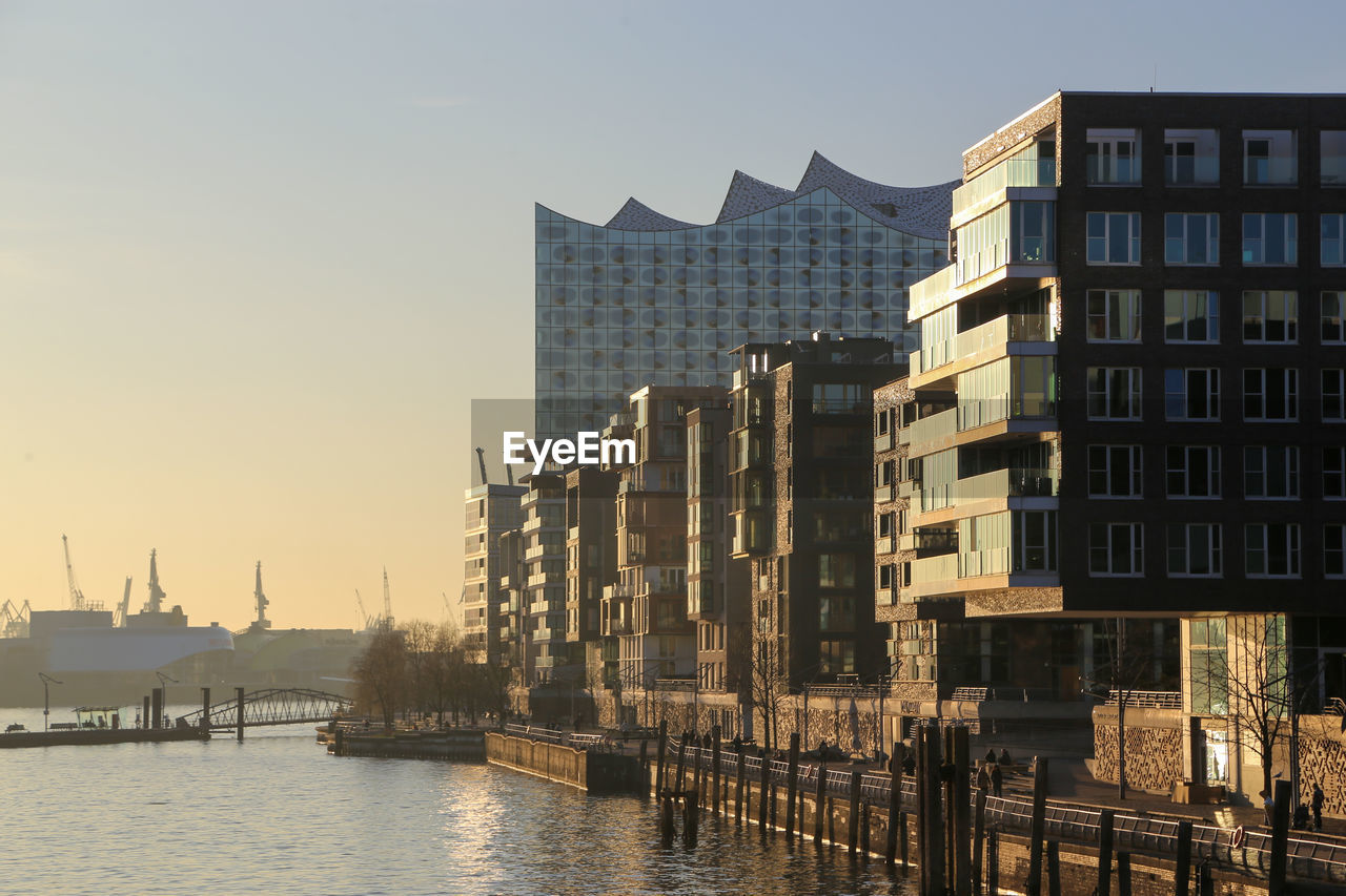 View of buildings by river against sky in city