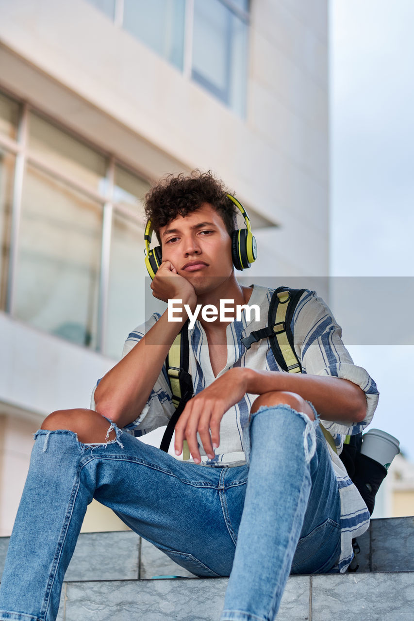 Boring young afro with headphones on sitting on the street