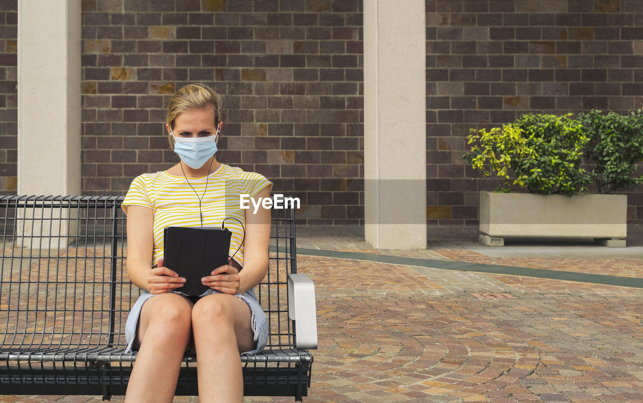 Woman wearing mask using digital tablet outdoors