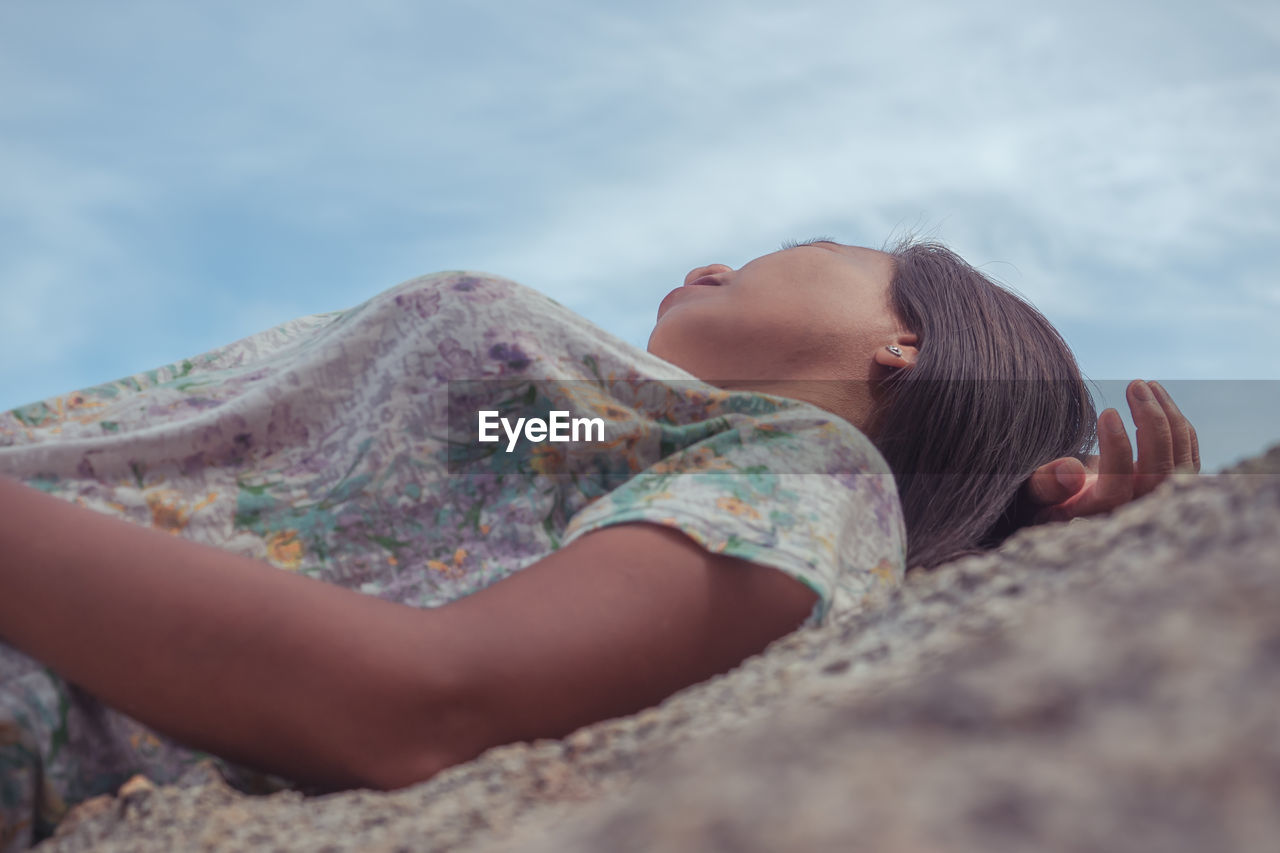 Midsection of woman lying on rock against sky