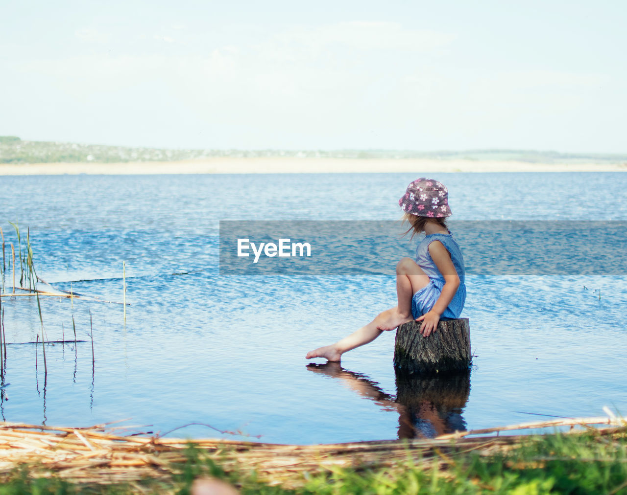 Girl sitting on wooden post in lake against sky