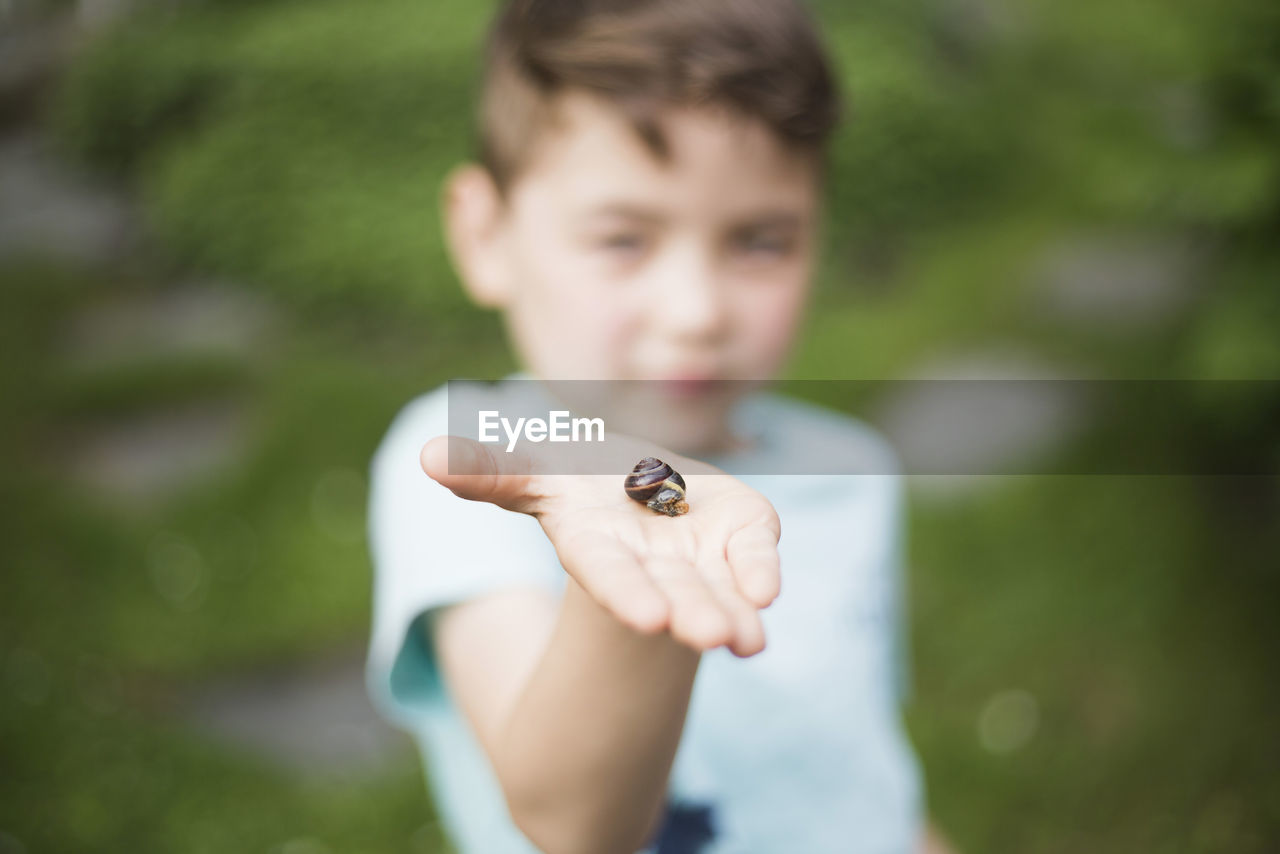 Boy showing snail on palm in back yard