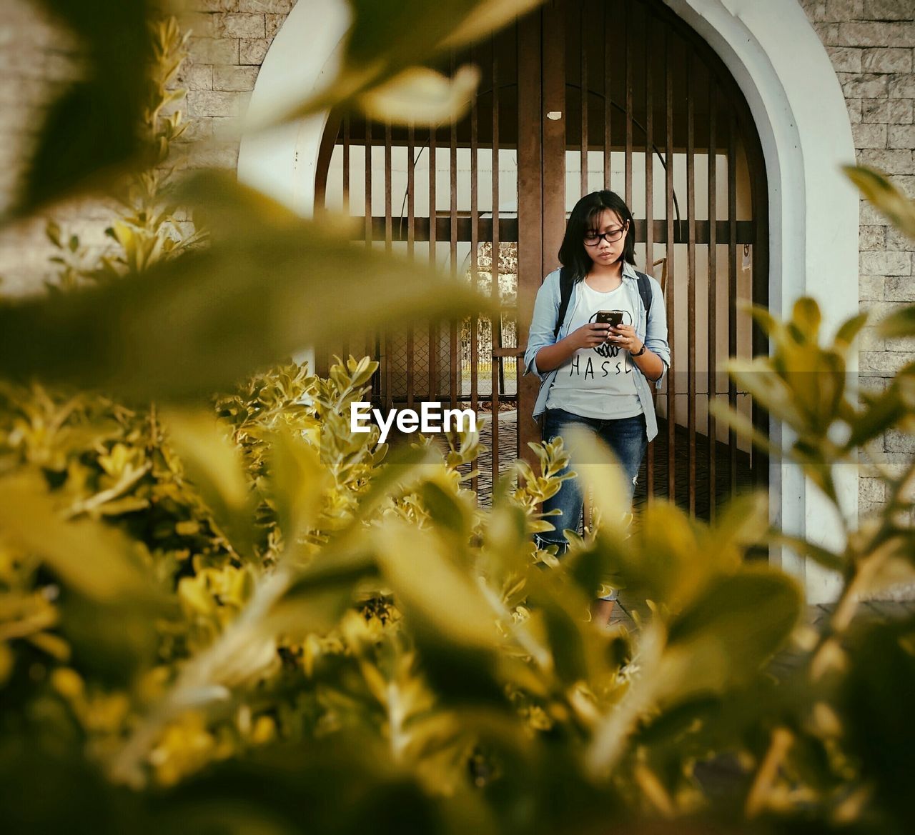 Young woman using smart phone standing against gate