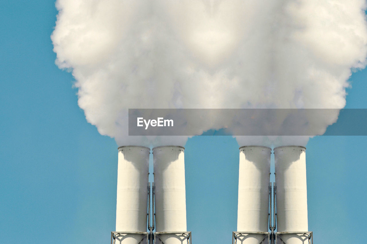 Low angle view of smoke emitting from chimneys against clear sky