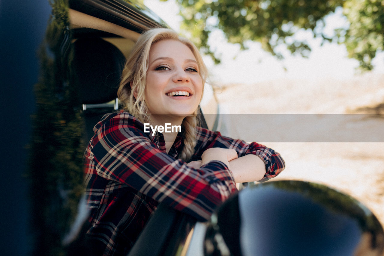 PORTRAIT OF SMILING YOUNG WOMAN SITTING ON TREE