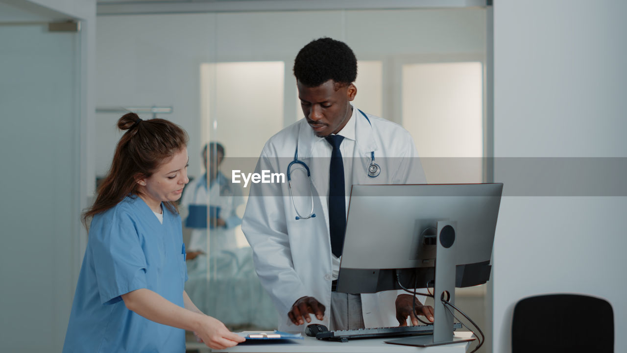 Nurse showing file folder to doctor at desk in hospital