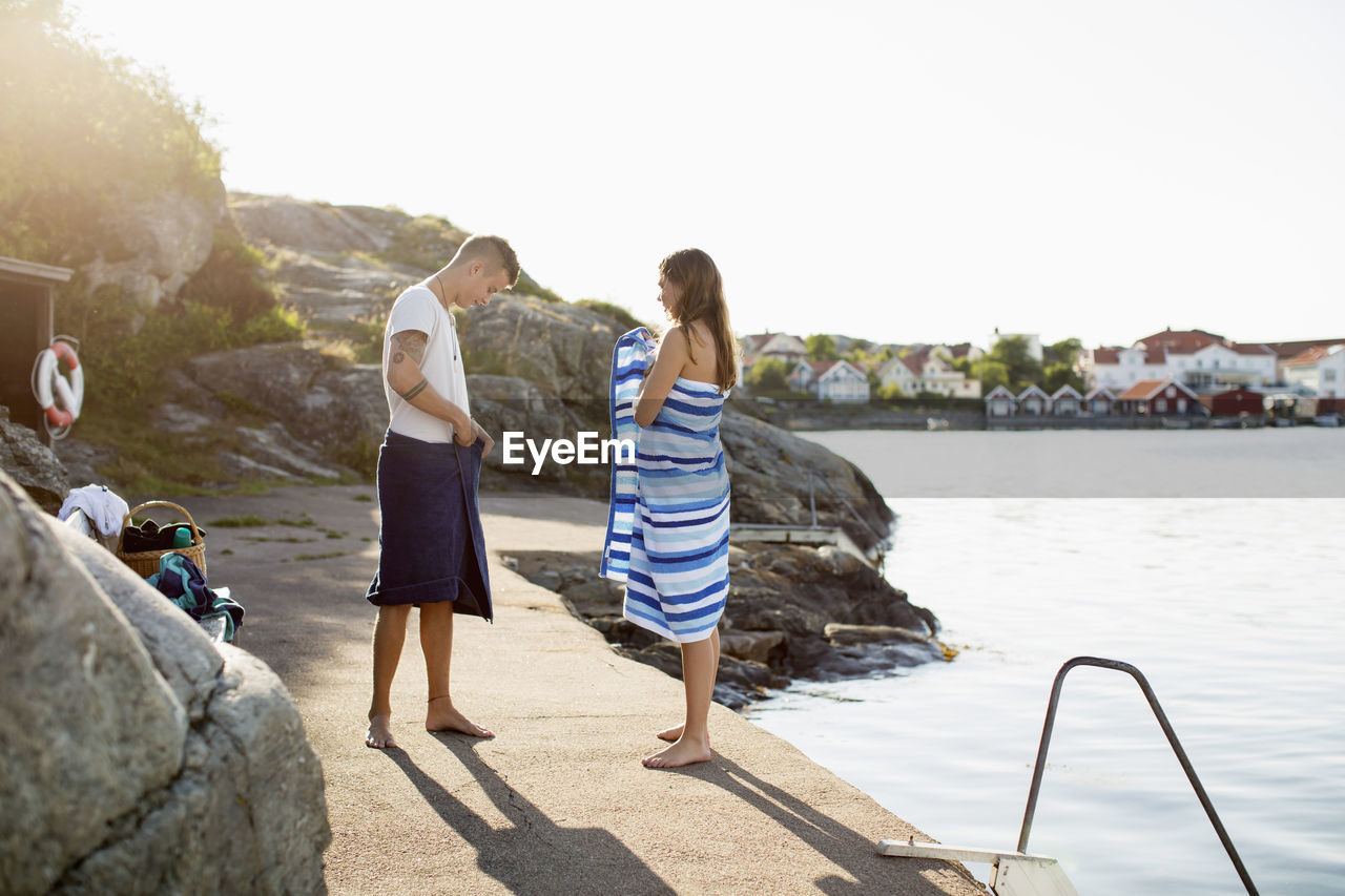 Full length of couple wrapping themselves in towel at lakeshore