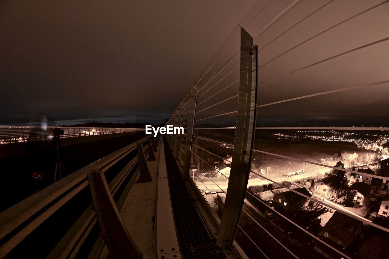 HIGH ANGLE VIEW OF BRIDGE OVER CITY AGAINST SKY AT NIGHT