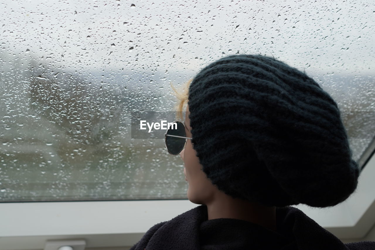 Portrait of woman looking through window during rainy season