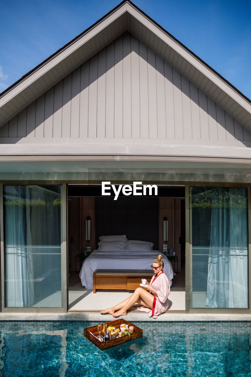 Full length of woman sitting in house by swimming pool