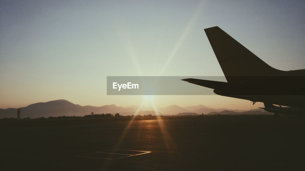 Silhouette airplane on runway against sky during sunset