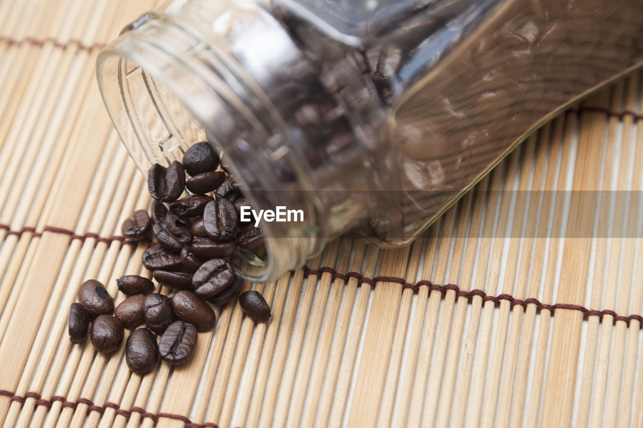 Roasted coffee beans spilling from jar on place mat