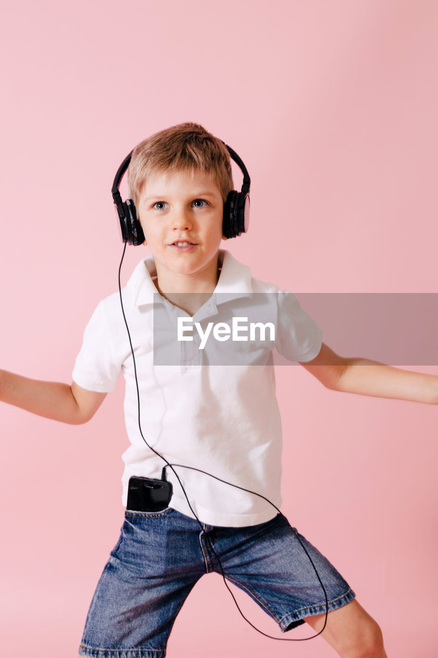 Boy listening music on headphones while standing against colored background