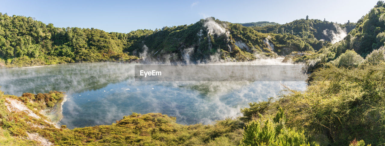 Panoramic view on huge boiling geothermal lake surrounded by lush green foliage, new zealand