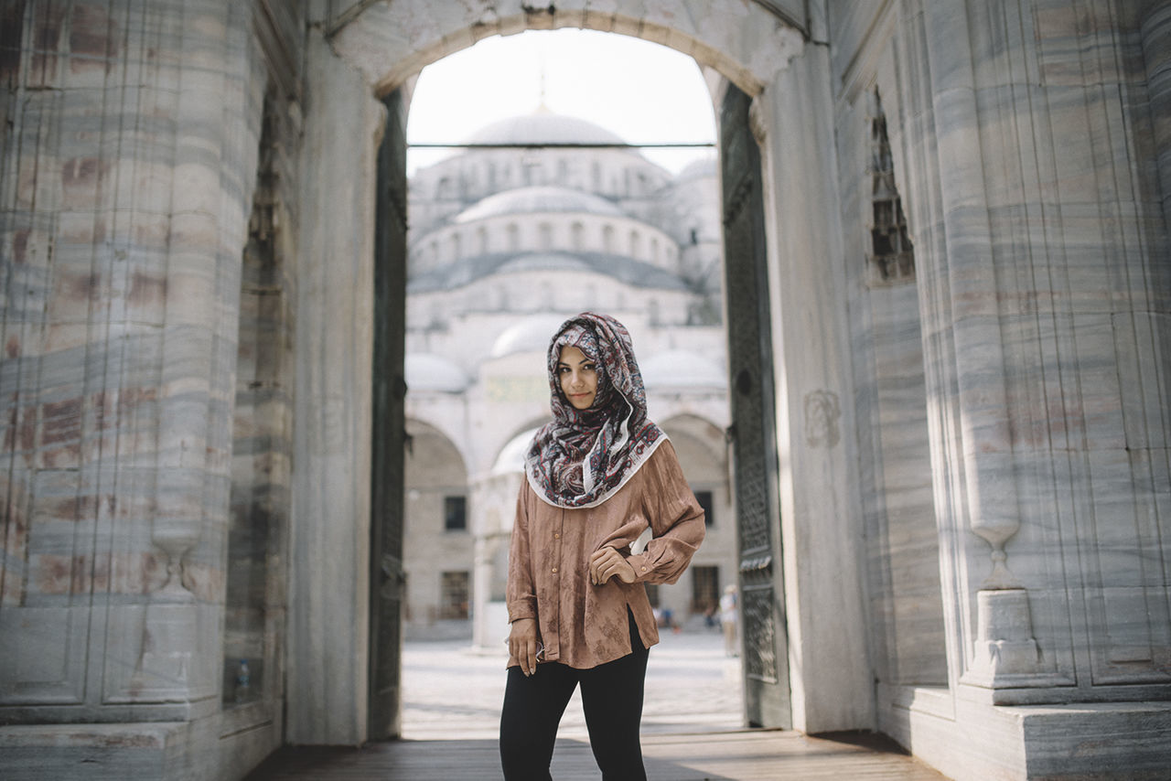Portrait of confident woman with hand on hip wearing hijab while standing against built structure