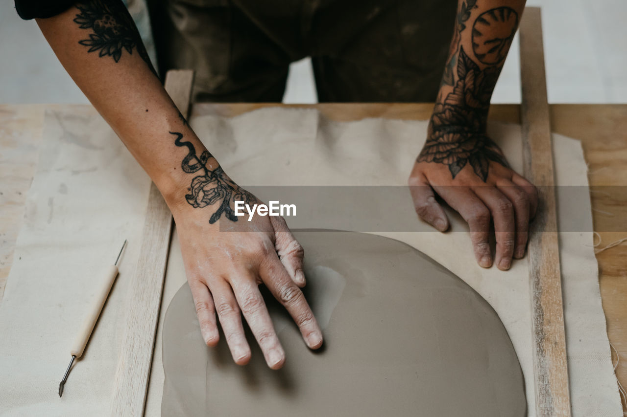 Artisan using sharp tool and making holes in piece of clay while creating handmade pottery in art studio