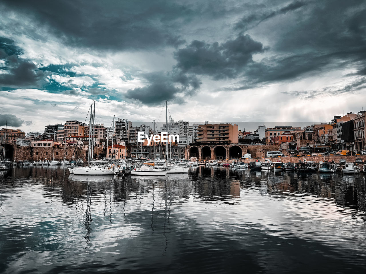 Buildings by sea against cloudy sky