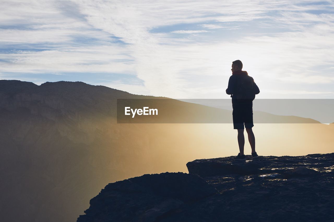 Man standing at cliff against sky during sunset