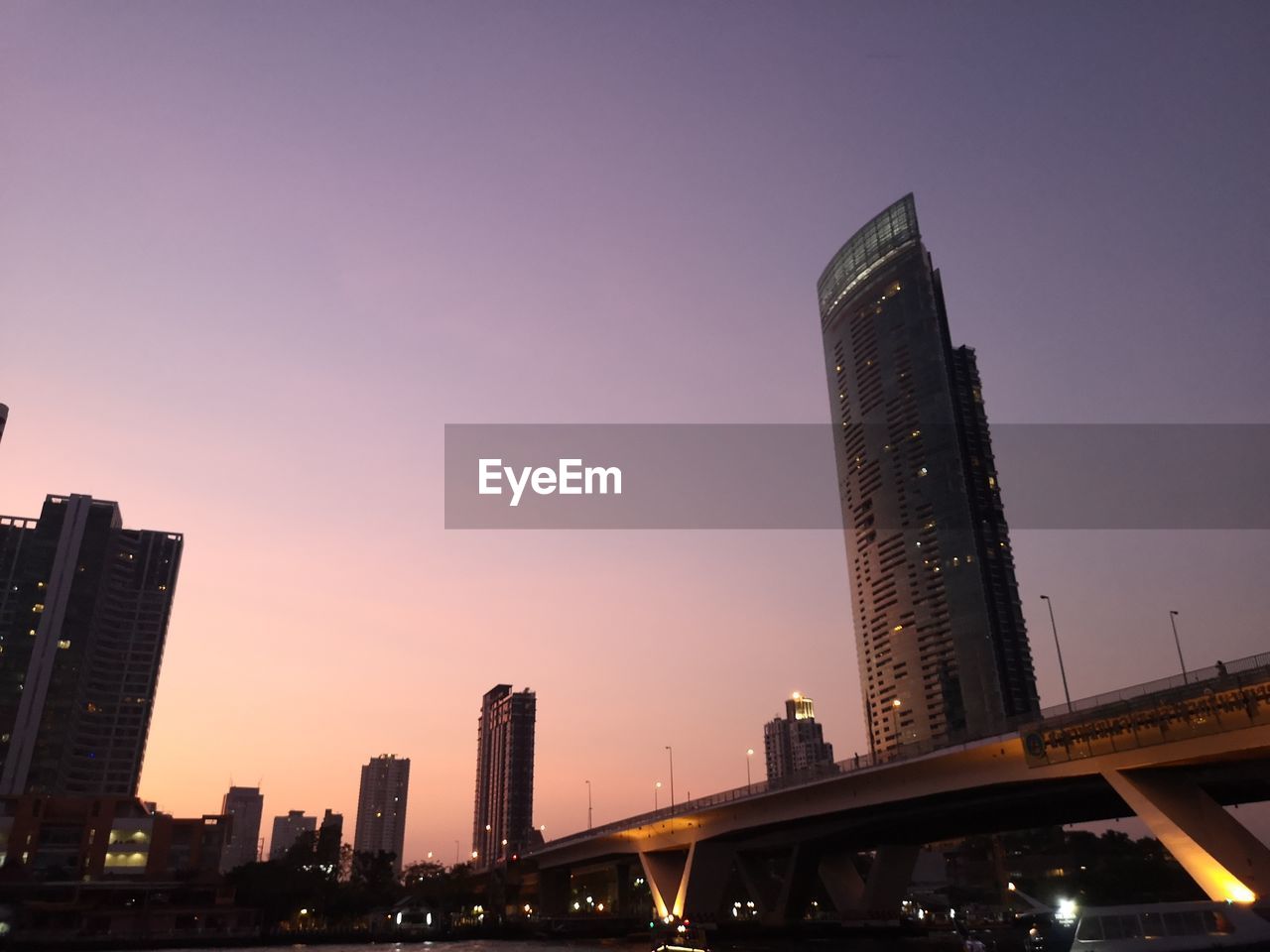 LOW ANGLE VIEW OF ILLUMINATED BRIDGE AND BUILDINGS AGAINST SKY DURING SUNSET