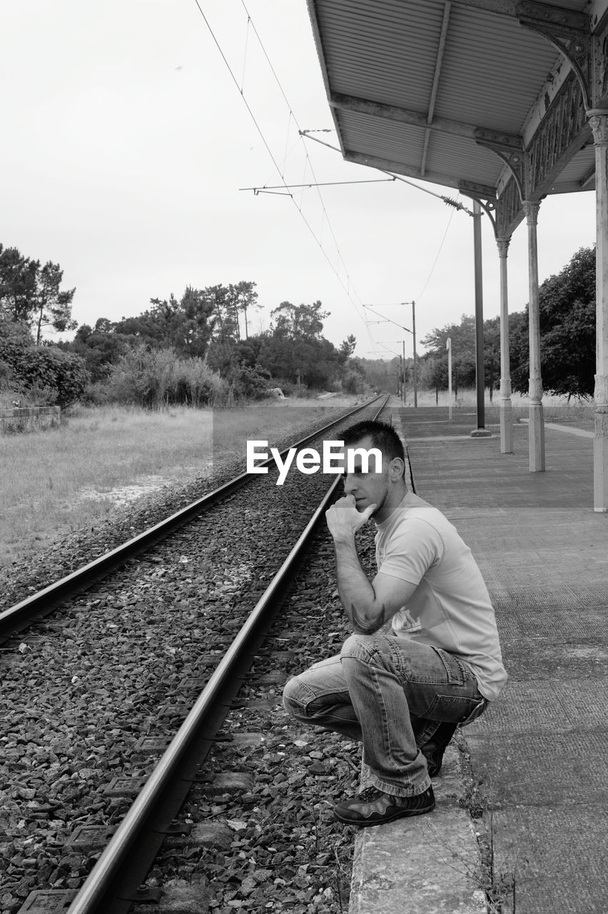 Thoughtful young man crouching on railroad station platform