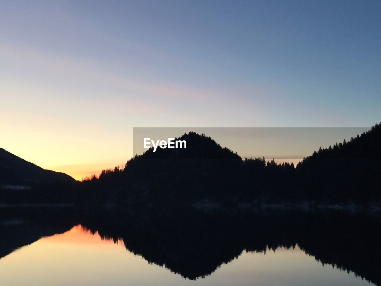 Silhouette mountains by lake against clear sky at sunrise