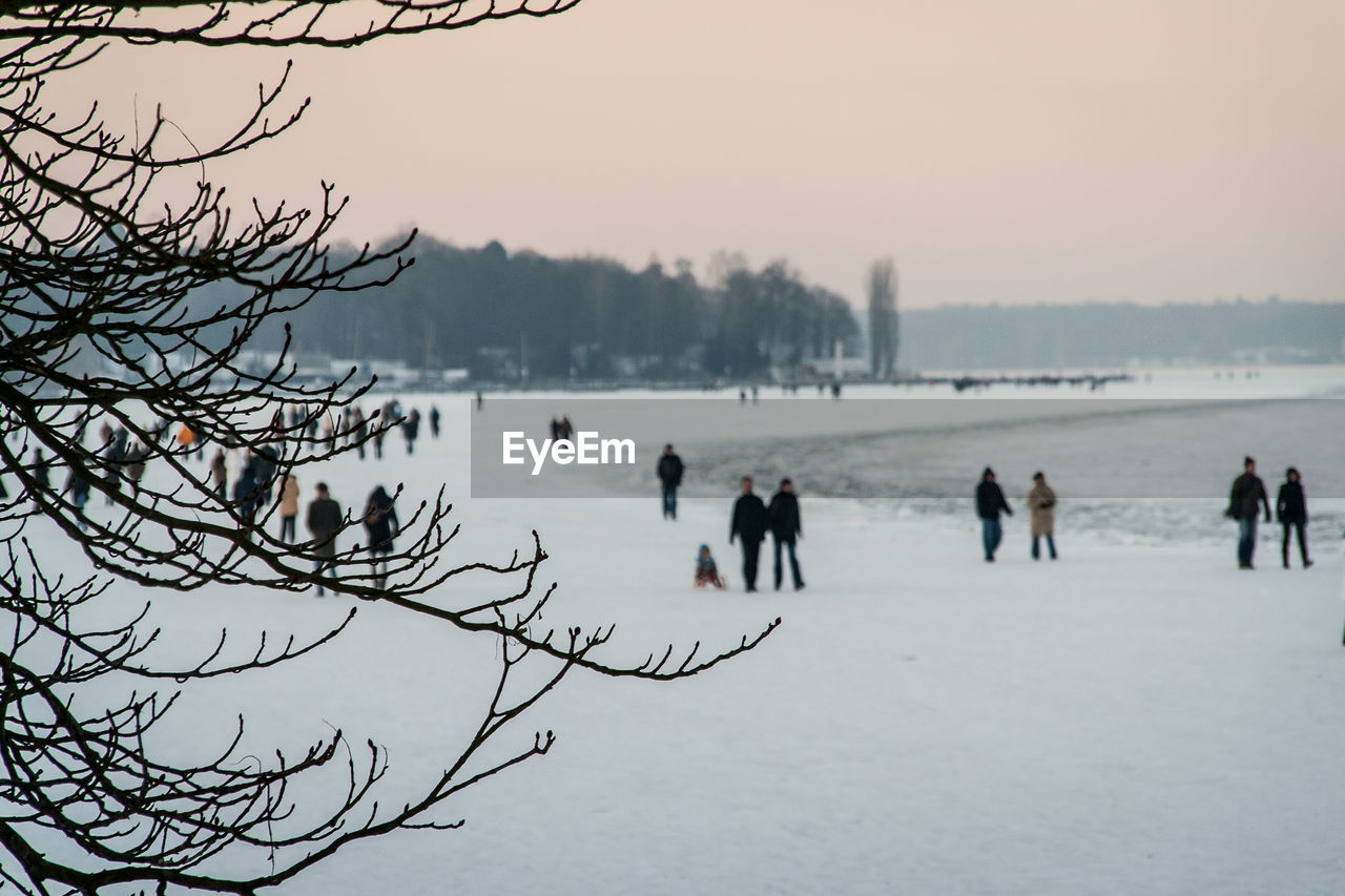 Tourists walking on snow covered landscape during sunset