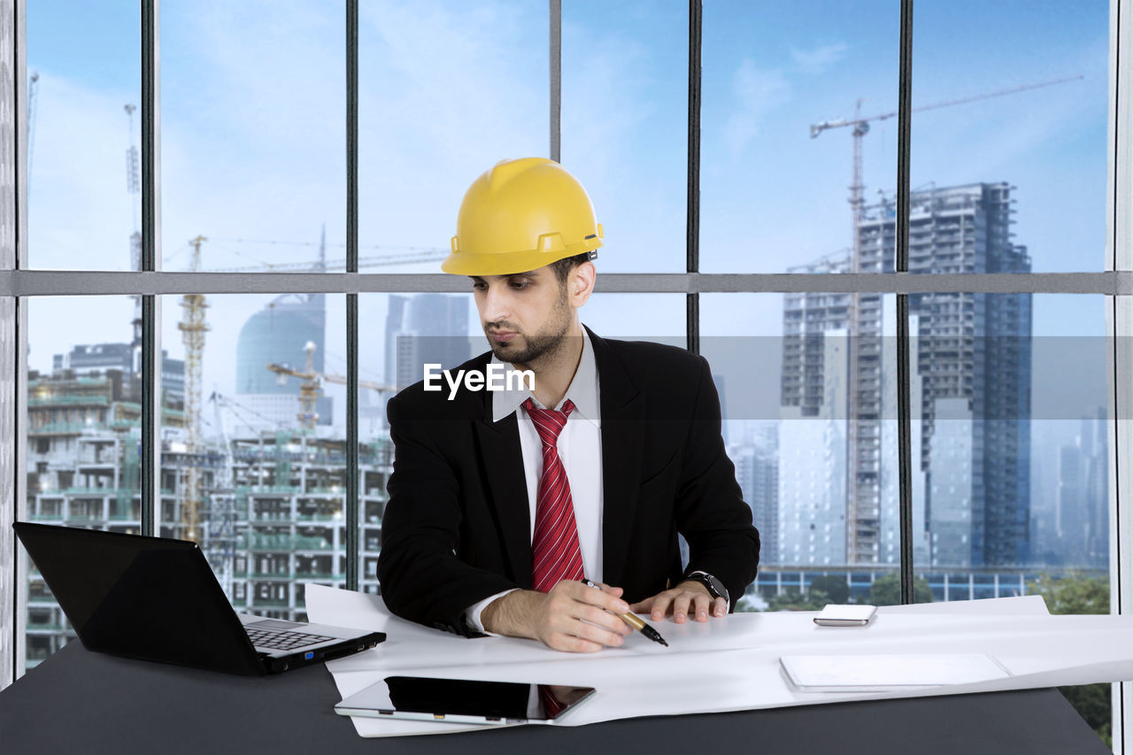 Architect wearing suit and yellow hardhat working in office