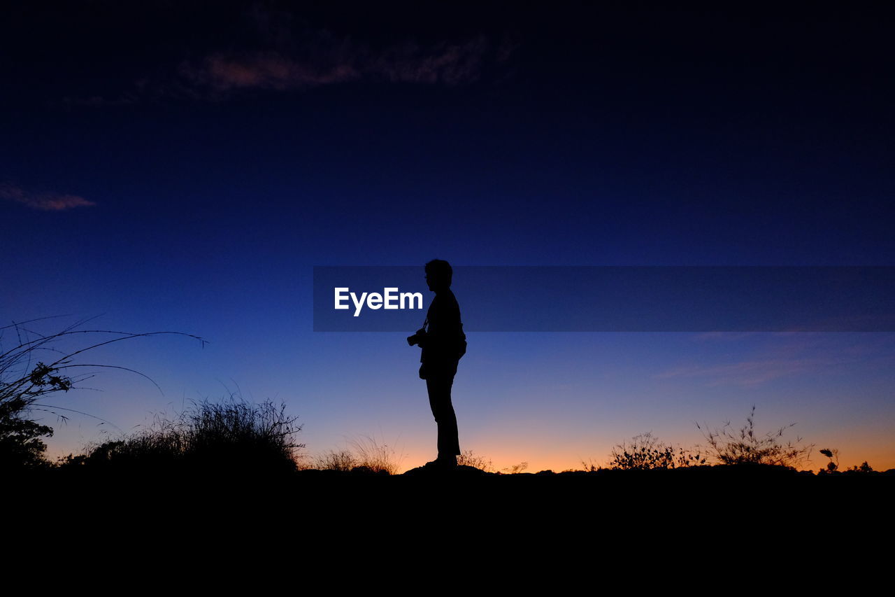 Silhouette man standing on land against sky during sunset