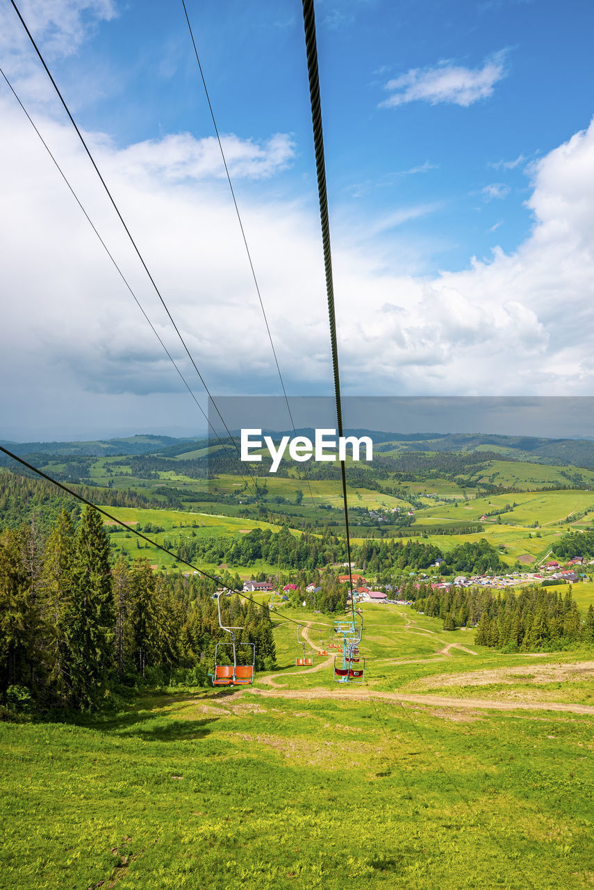 Empty ski lifts over beautiful green grassy covered hill against cloudy sky