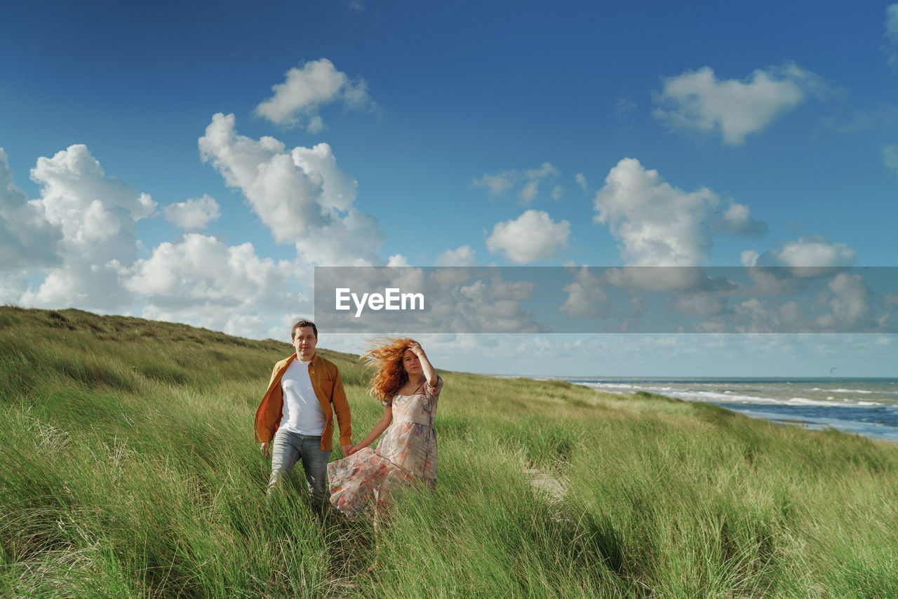 Couple on field by sea against sky