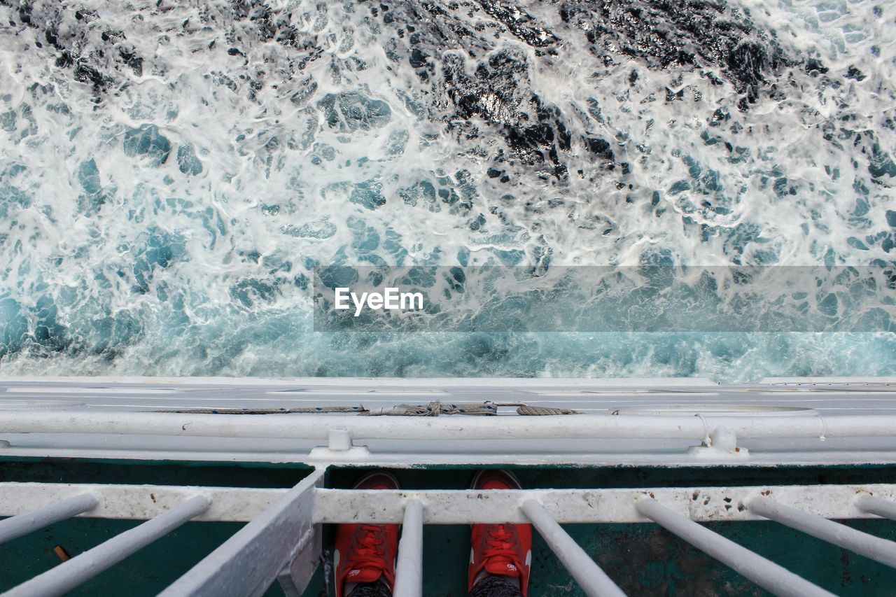 Low section of man standing by railing in boat over sea