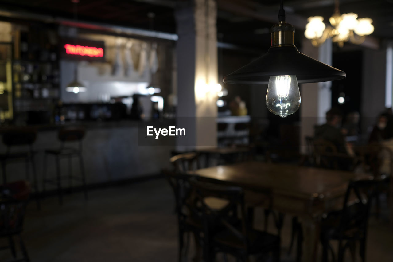 lighting equipment, illuminated, table, restaurant, business, cafe, electric lamp, night, indoors, seat, bar, food and drink, lighting, chair, electric light, furniture, architecture, focus on foreground, food and drink industry, room, light, light - natural phenomenon, no people, pendant light