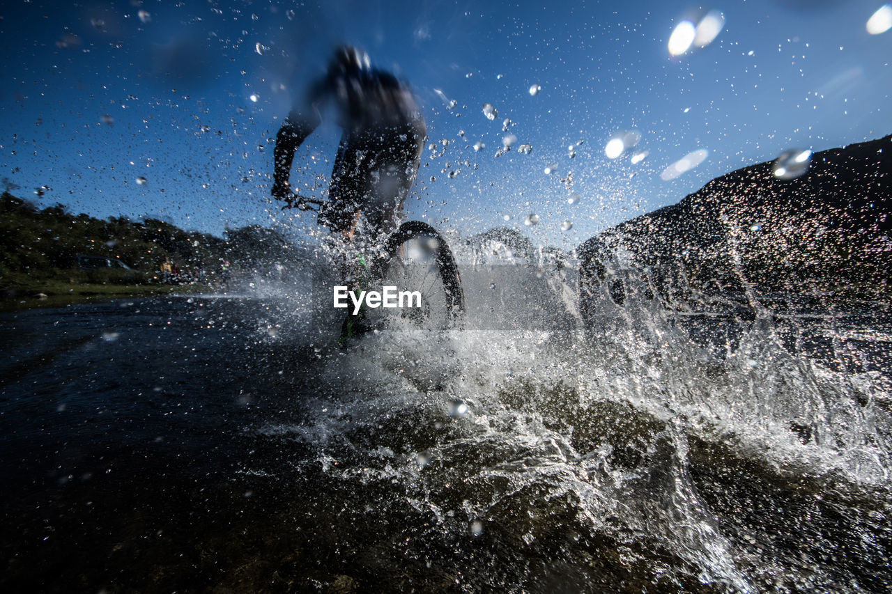 Rear view of man riding bicycle in water at shore