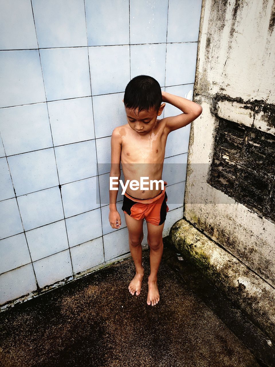 Full length of shirtless boy showering against tiled wall