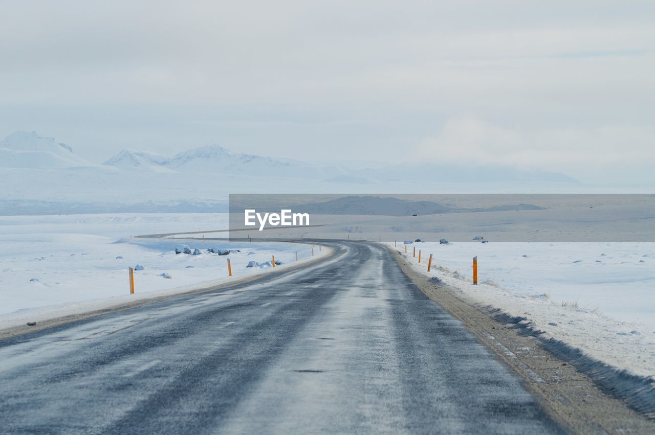 Road leading towards snowcapped mountains against sky