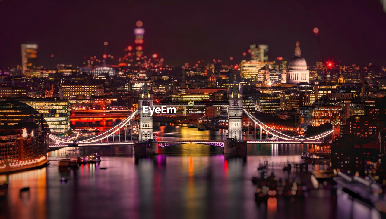 Illuminated bridge over river in city at night